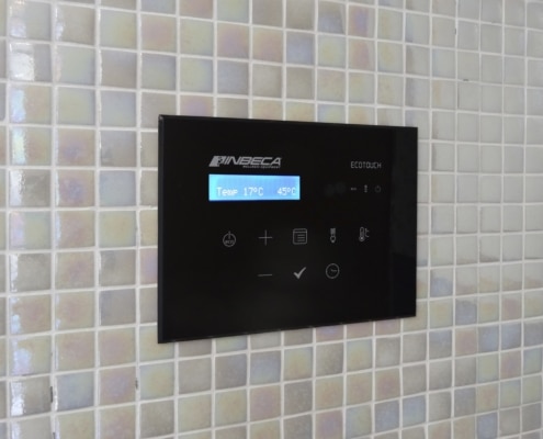 Panel de control de color negro en un baño de vapor de gresite gris con la marca Inbeca