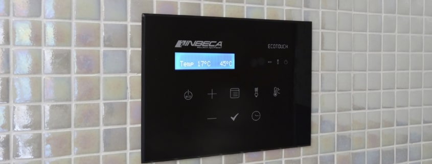 Panel de control de color negro en un baño de vapor de gresite gris con la marca Inbeca